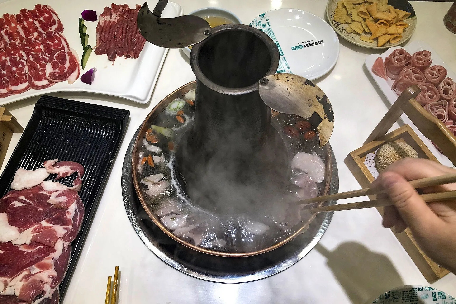 湯気の立つ北京の銅鍋（煙突付き）の涮羊肉と、薄切りラムの皿