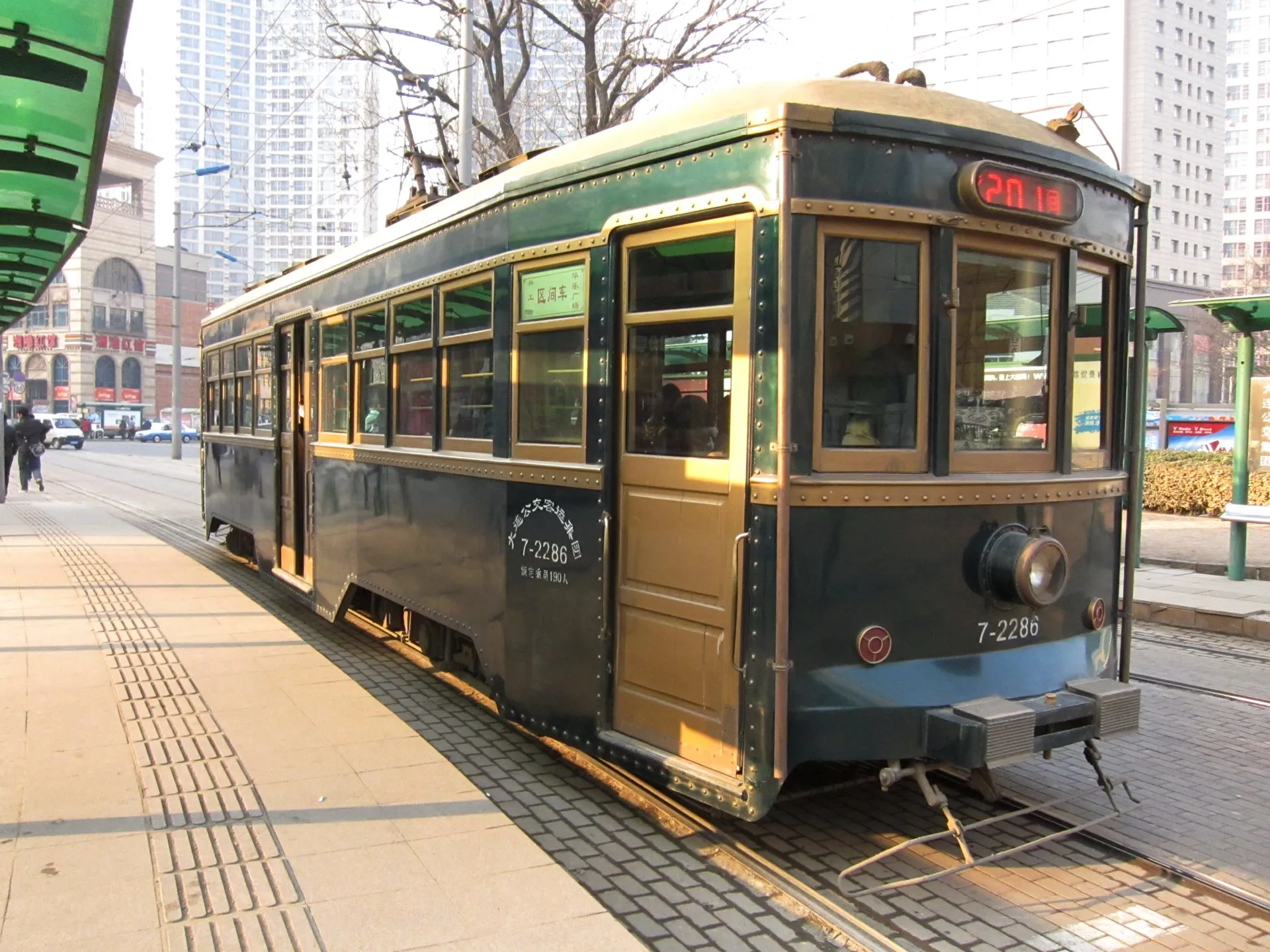 A vintage teal-and-cream Dalian tram waiting at a city-centre stop